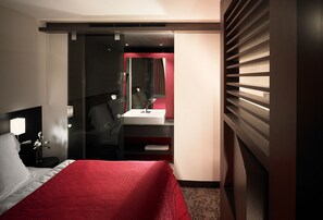 A hotel room with a bed, a desk, a mirror, and a vanity. - Hotel International (Clervaux)