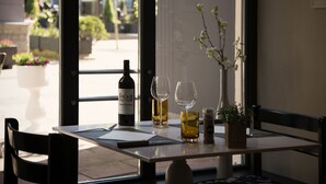 A table set for two with a bottle of wine, two wine glasses, a vase with flowers, and a small plant on a table in a restaurant. - Hotel International (Clervaux)