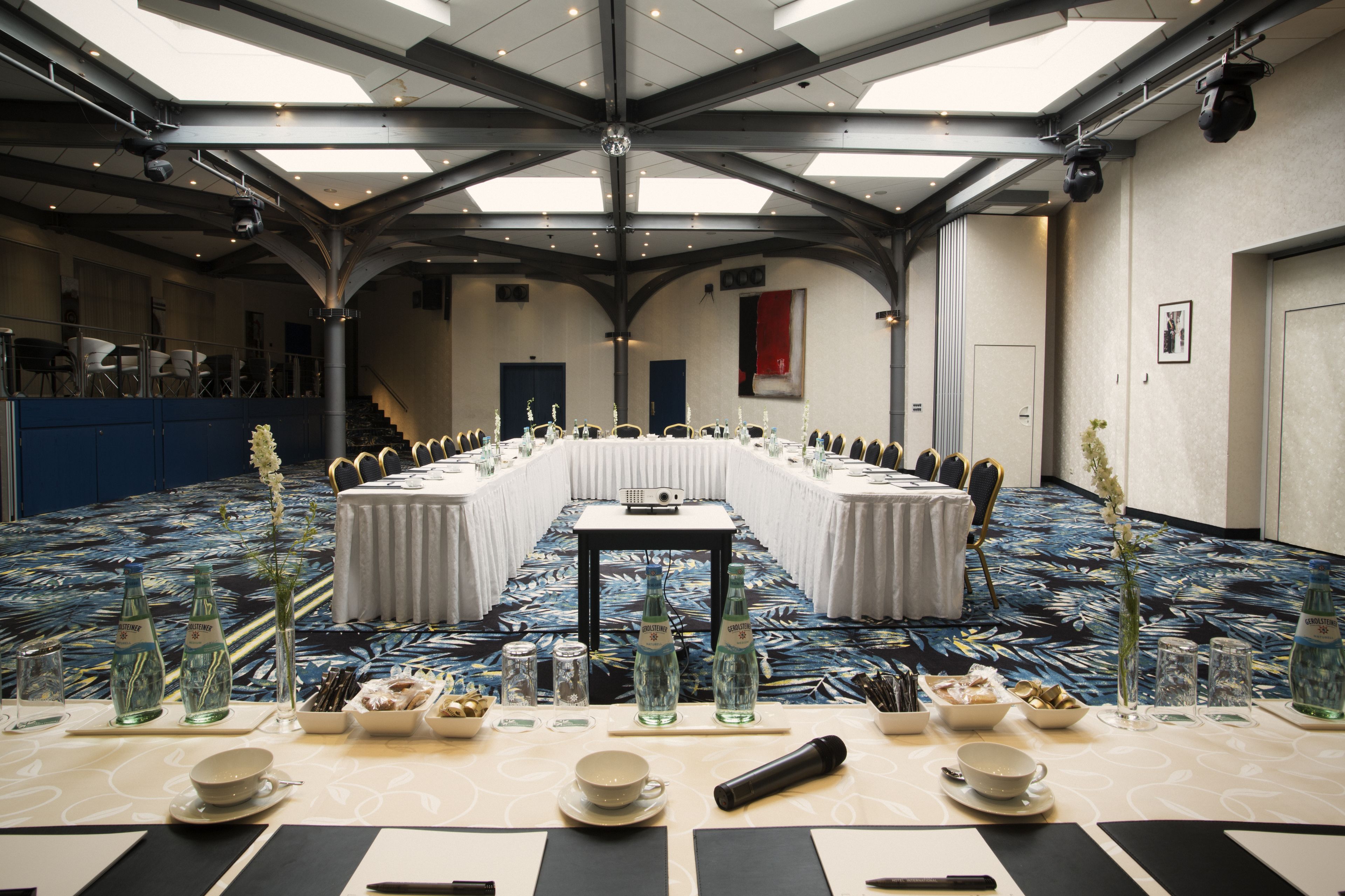 Ein Konferenzraum mit einem langen Tisch, der für ein Meeting vorbereitet ist, ausgestattet mit Wasserflaschen, Gläsern und einem Projektor.