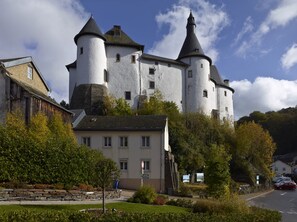 A castle-like building with multiple towers and a white facade, surrounded by greenery and a parking area. - Hotel International (Clervaux)