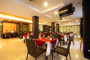 A restaurant with tables set for dining, a reception area, and a TV mounted on the wall. - Baramee Hip Hotel (Patong)