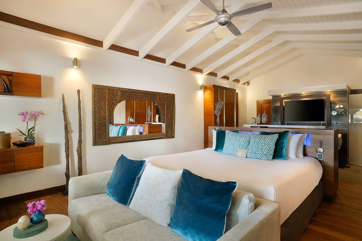 A modern hotel room with a large bed, a sofa, a TV, and a ceiling fan.