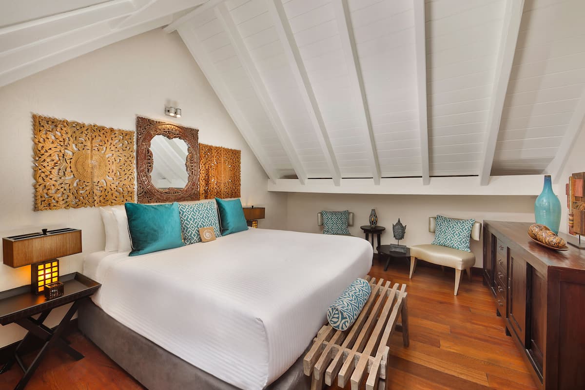 A spacious bedroom with a large bed, a wooden bench, a desk, and a dresser.