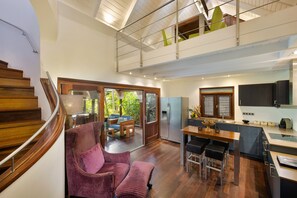 A modern kitchen with a dining area, wooden staircase, and a view of the outdoors.