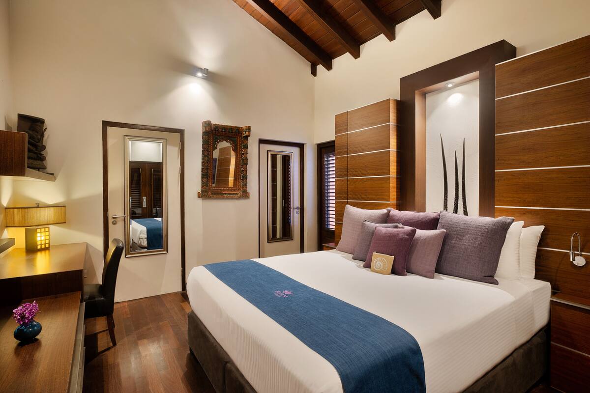 A hotel room with a large bed, a desk with a lamp, a chair, and a mirror.