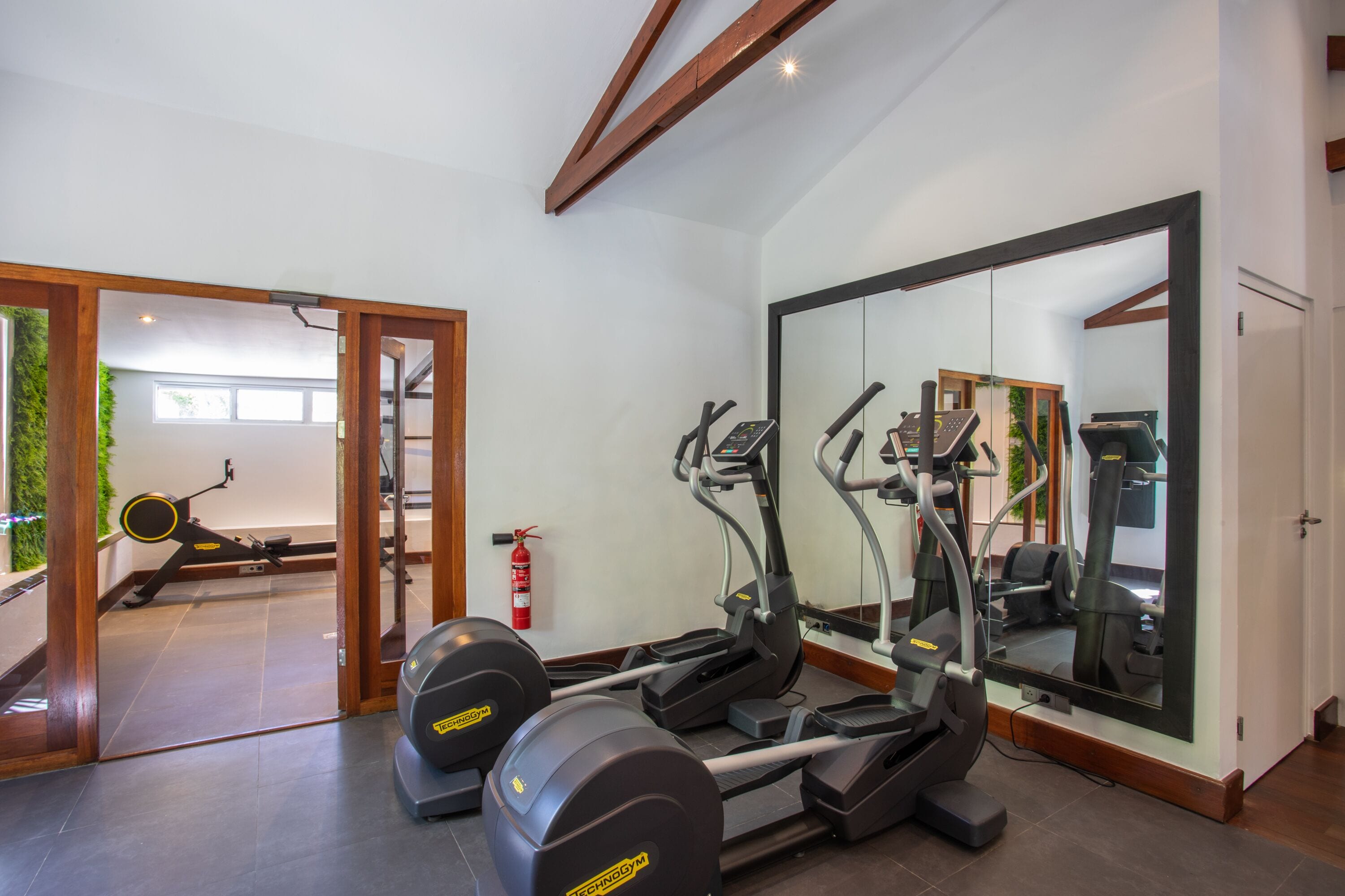 A gym with cardio machines, a mirror, and a fire extinguisher.