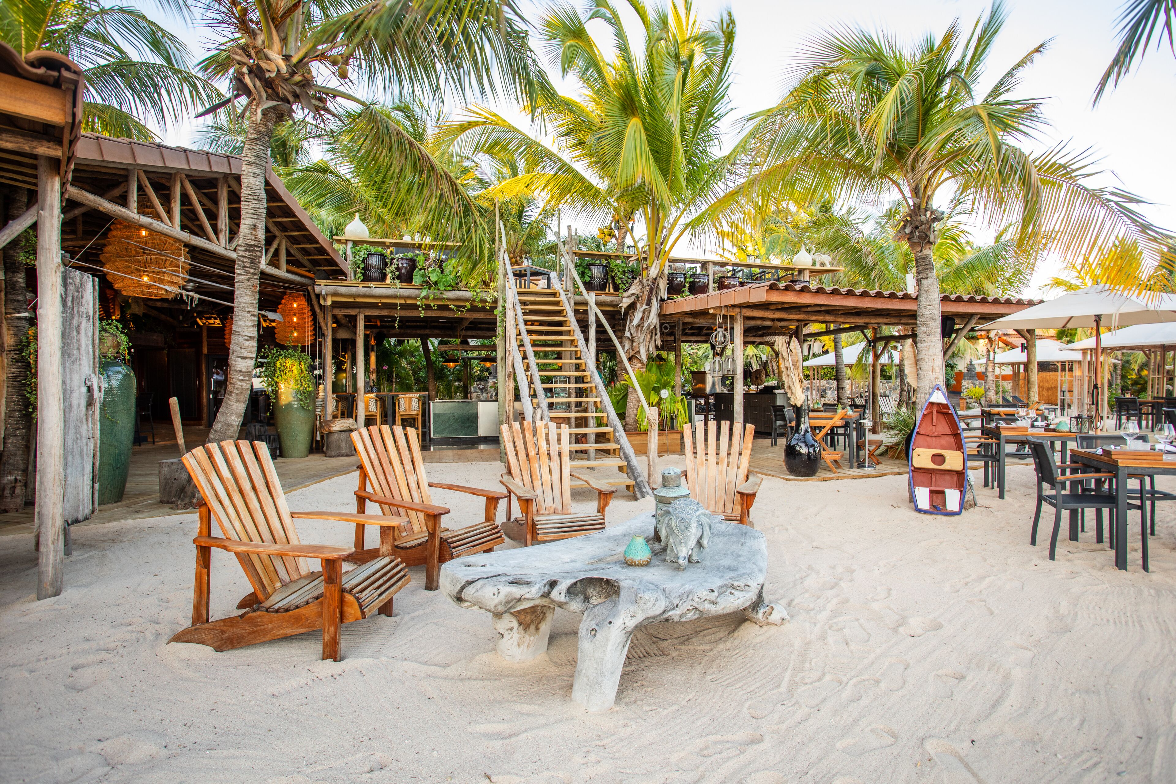 A beachside restaurant with wooden chairs, a large table, and a boat sculpture.