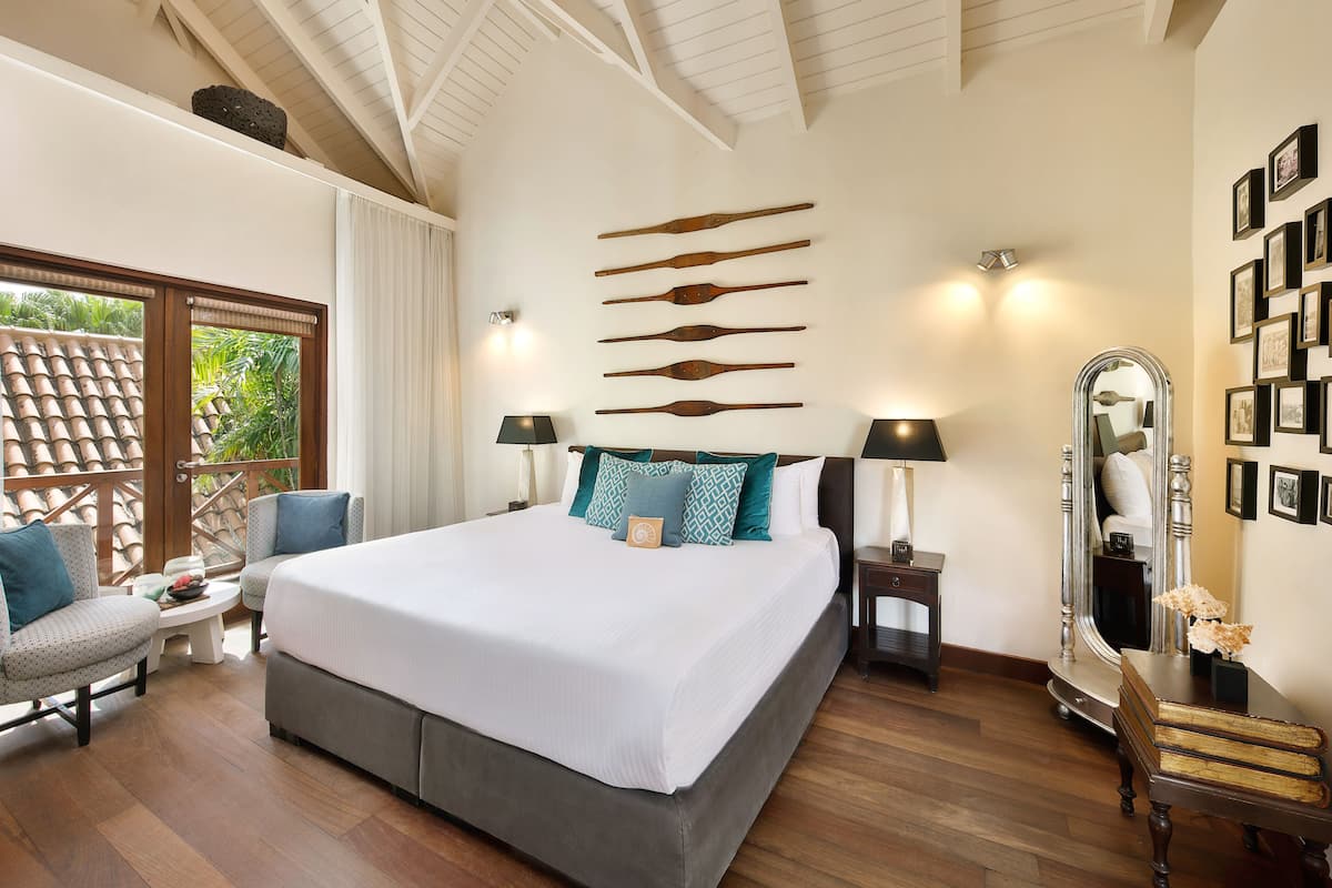 A spacious bedroom with a large bed, two bedside tables with lamps, a mirror, and a wall with framed pictures.