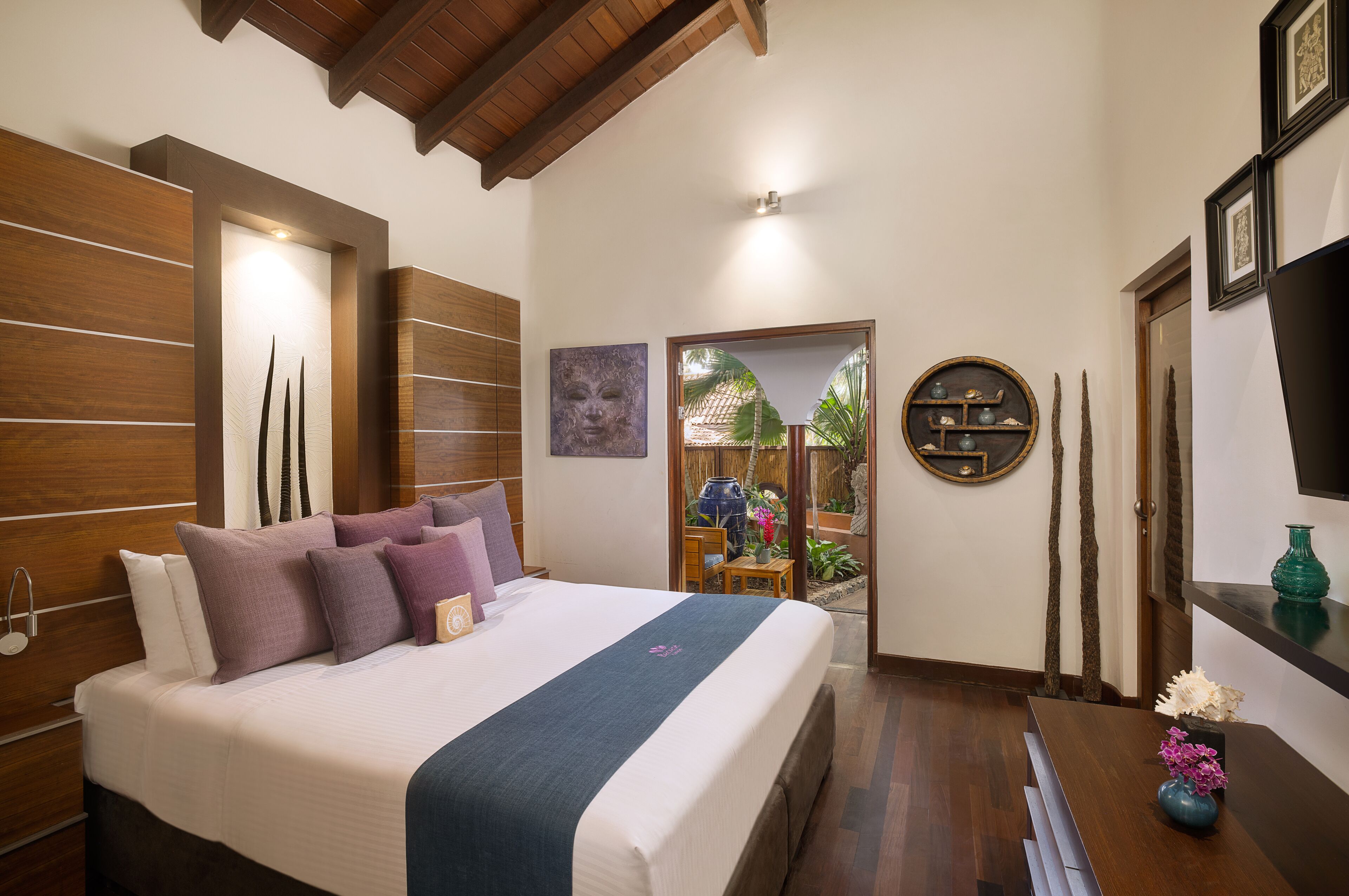 A hotel room with a large bed, wooden panel walls, a small table with a vase, and a view of the outdoors.