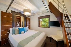 A modern hotel room with a large bed, a wooden headboard, a TV mounted on the wall, a window with a view of greenery, and a staircase.