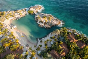 An aerial view of a coastal resort with multiple bungalow-style accommodations, a sandy beach, and clear turquoise waters. - Baoase Curacao (Willemstad)