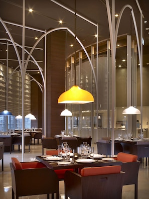 A modern restaurant interior with high ceilings, arched lighting fixtures, and a view of the cityscape through large windows.