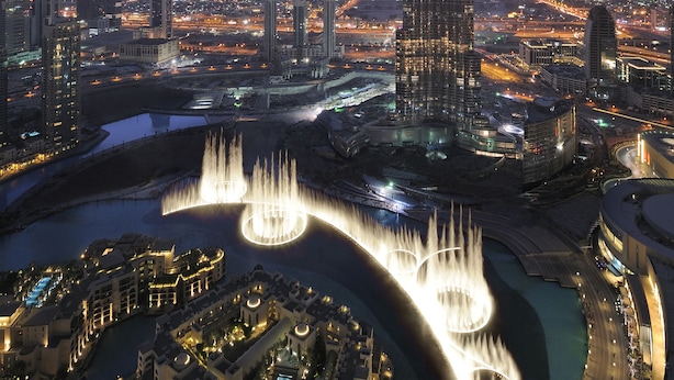 A cityscape with a prominent skyscraper, a waterfront area with fountains, and surrounding buildings.