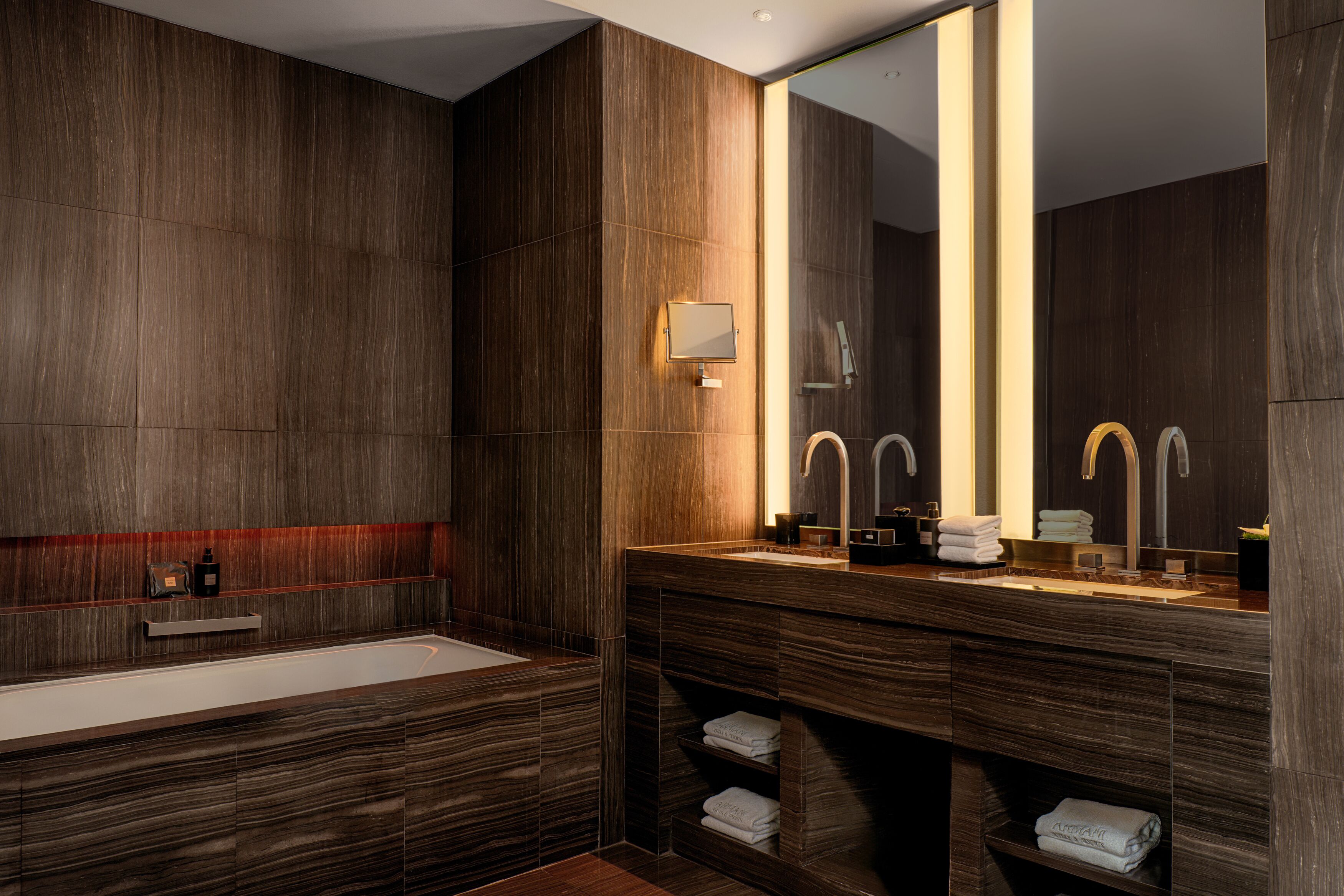 Een moderne badkamer met een grote spiegel, dubbele wastafels en een inbouwplank met handdoeken.