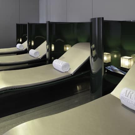 A row of reclining massage chairs with towels, each with a small table and a lamp.