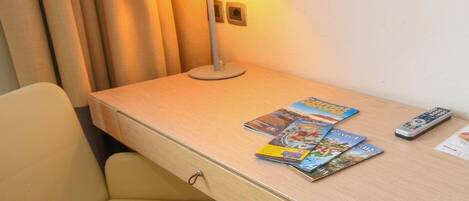 Une chambre d’hôtel avec un bureau en bois, une lampe, une télécommande et un magazine.