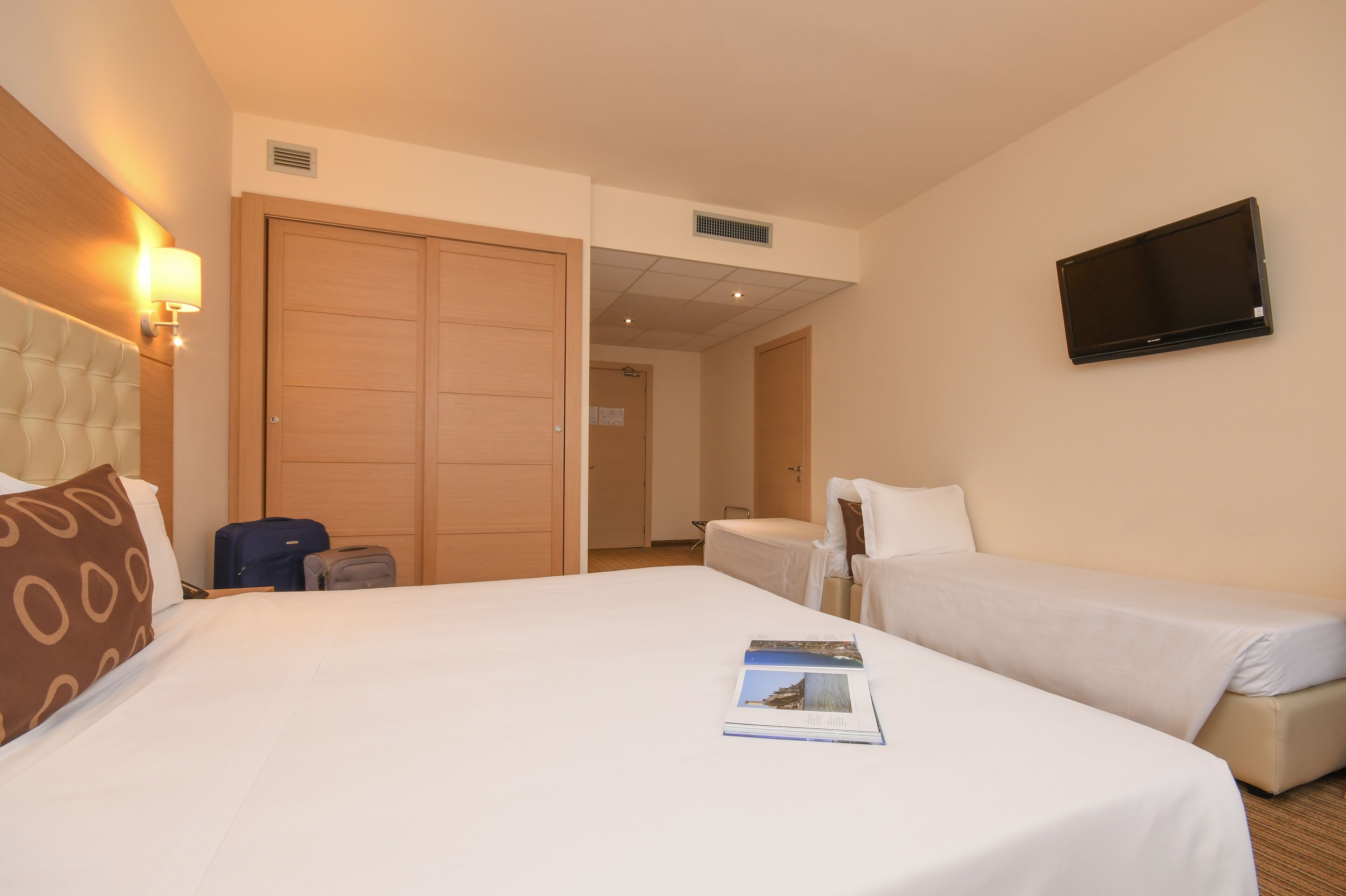 A hotel room with a large bed, a smaller bed, a TV mounted on the wall, and a wardrobe.
