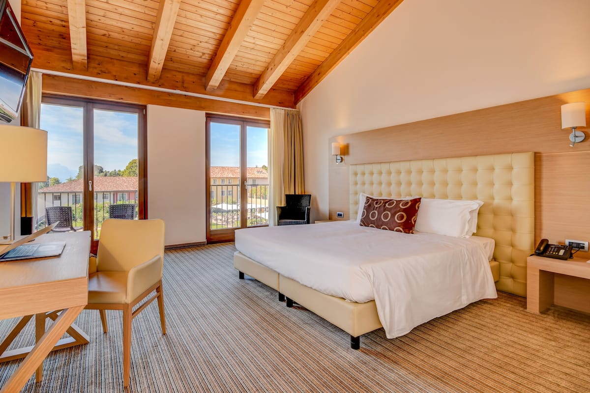 Een hotelkamer met een groot bed, een bureau en een stoel. Er is een raam met uitzicht op gebouwen.