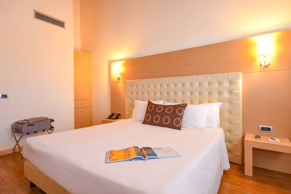 Een hotelkamer met een groot bed, nachtkastje, koffer en een aan de muur bevestigd telefoon.
