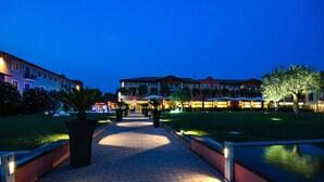 A well-lit pathway leading to a building with multiple balconies and a grassy area with trees. - TH Lazise - Hotel Parchi del Garda (Lazise)