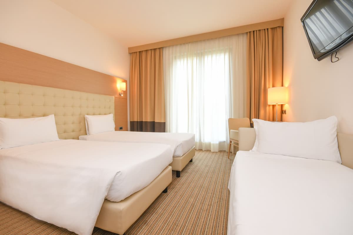 Een hotelkamer met twee bedden, een aan de muur bevestigde televisie en een groot raam met gordijnen.