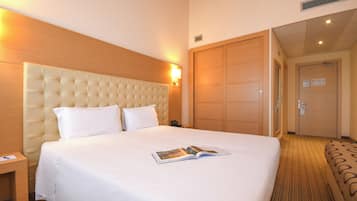 Una camera d'albergo con un letto grande, una testiera in legno, un comodino e una porta che dà su un'altra stanza.