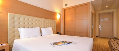 A hotel room with a large bed, a wooden headboard, a bedside table, and a door leading to another room.