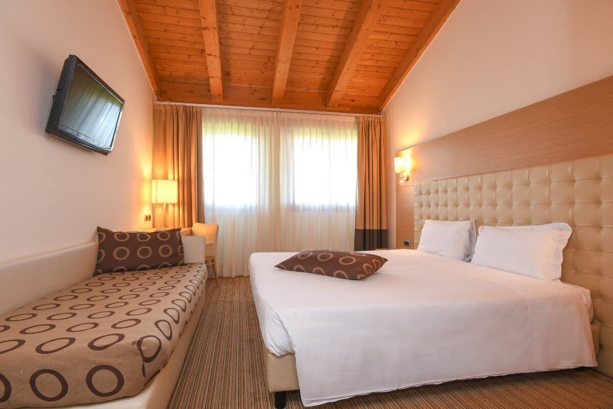 Een hotelkamer met een bed, een bank, een televisie en een raam met gordijnen.