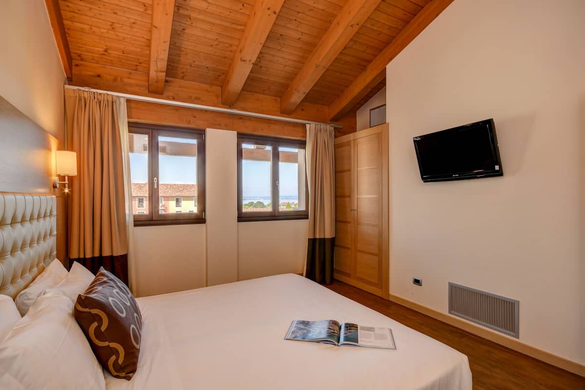 Een slaapkamer met een bed, een aan de muur bevestigde televisie en een raam met gordijnen.