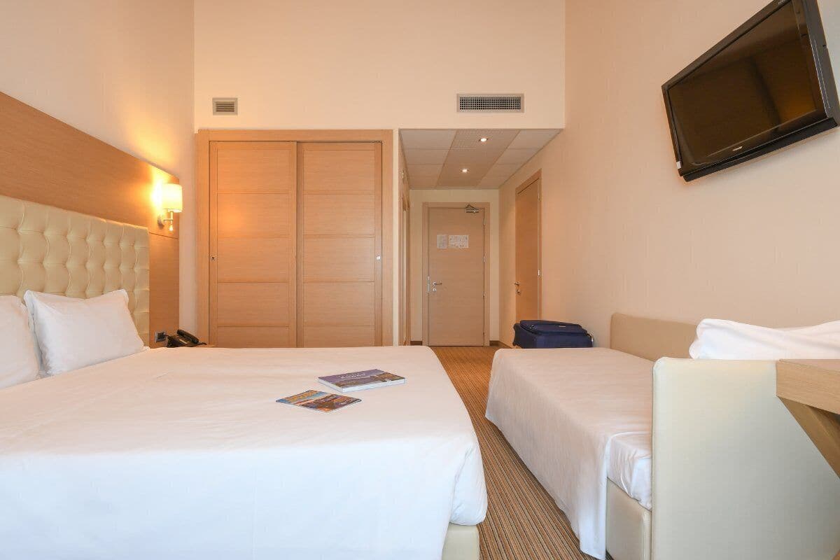 Een hotelkamer met twee bedden, een televisie en een deur die naar een andere kamer leidt.