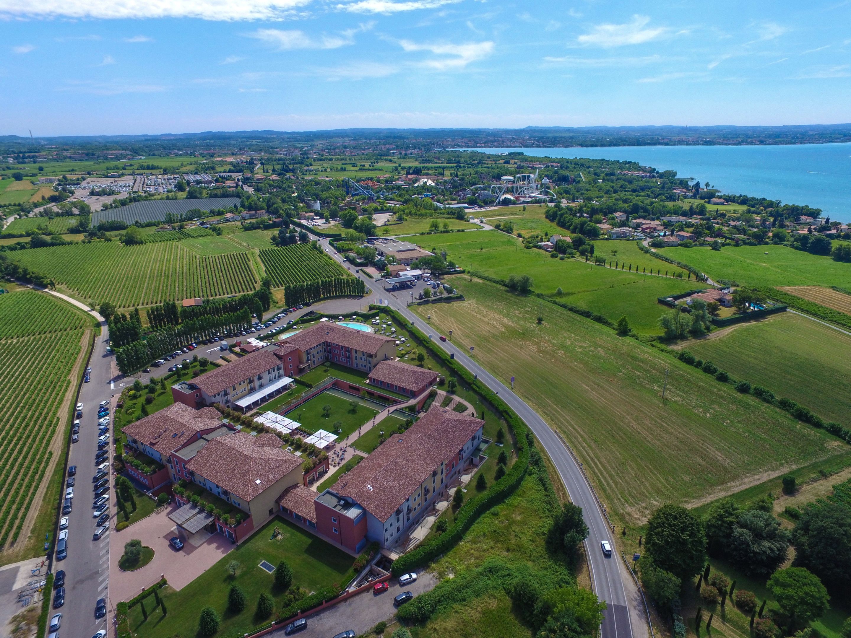 Vista aérea de un gran complejo con varias edificaciones, zonas de estacionamiento, campos verdes y un lago al fondo.