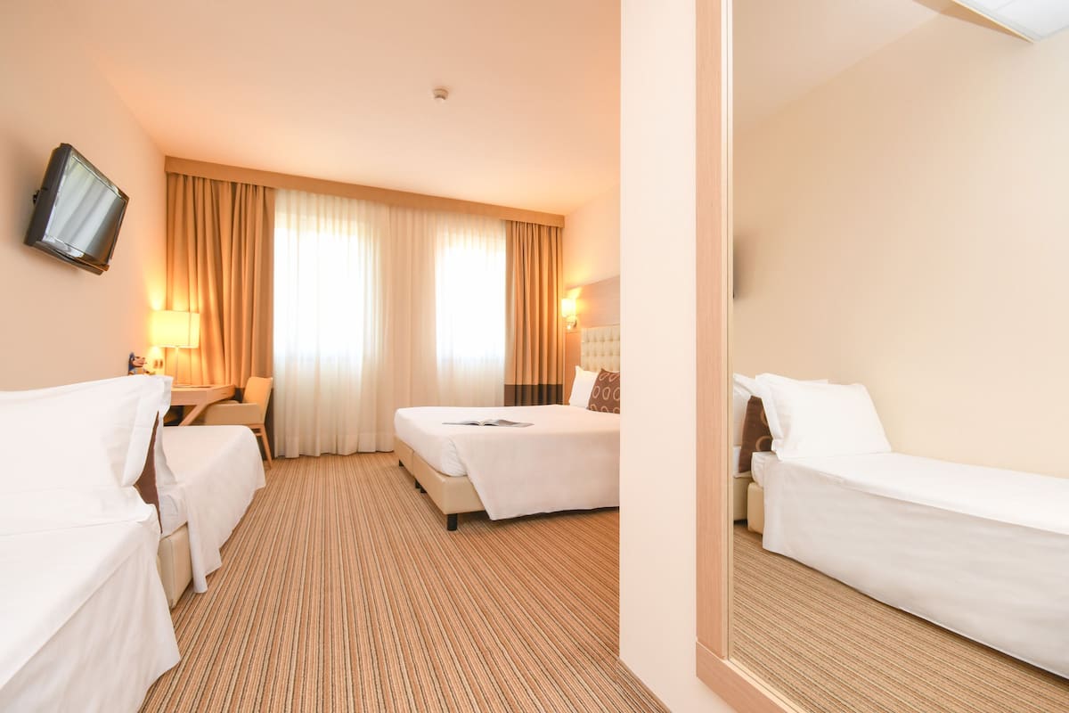 Hotelkamer met twee enkele bedden, een aan de muur bevestigde televisie, een bureau met stoel en een raam met gordijnen.