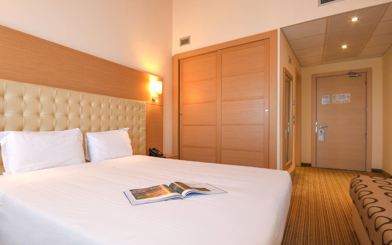 A hotel room with a large bed, a wooden headboard, a wardrobe, and a carpeted floor.