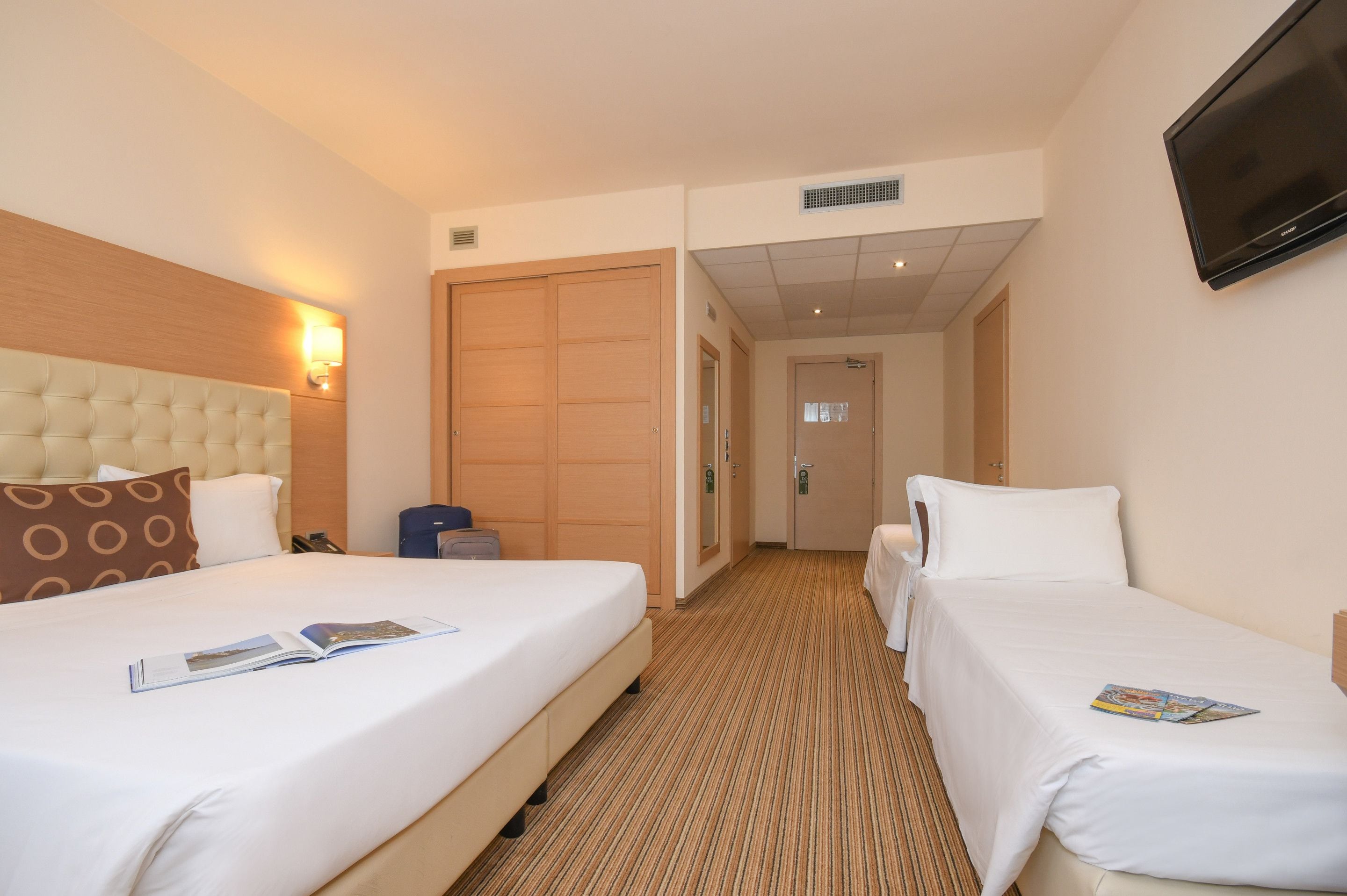 A hotel room with two beds, a large wooden headboard, a flat-screen TV, and a carpeted floor.