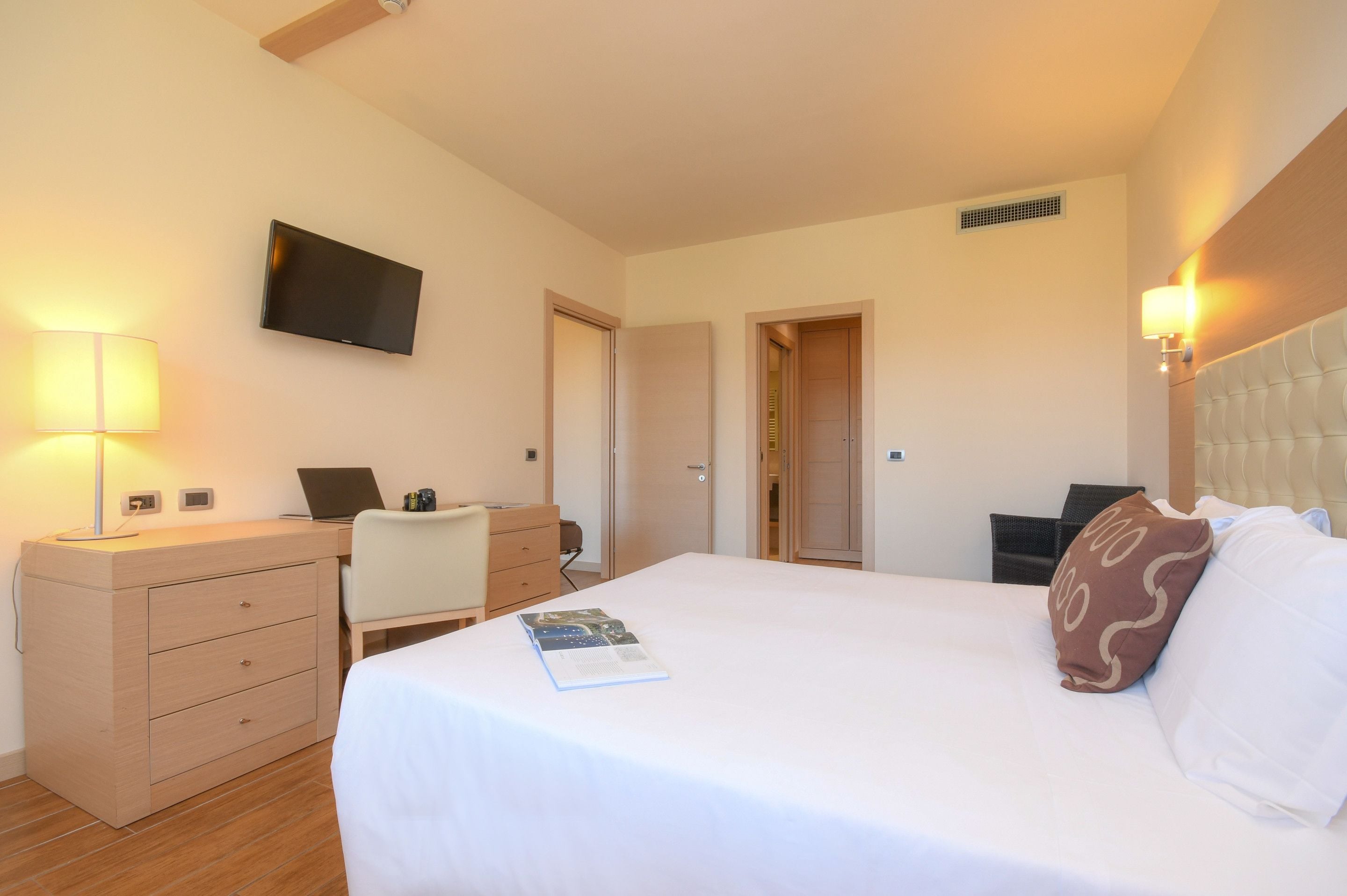 A hotel room with a bed, desk, chair, and a television on the wall.
