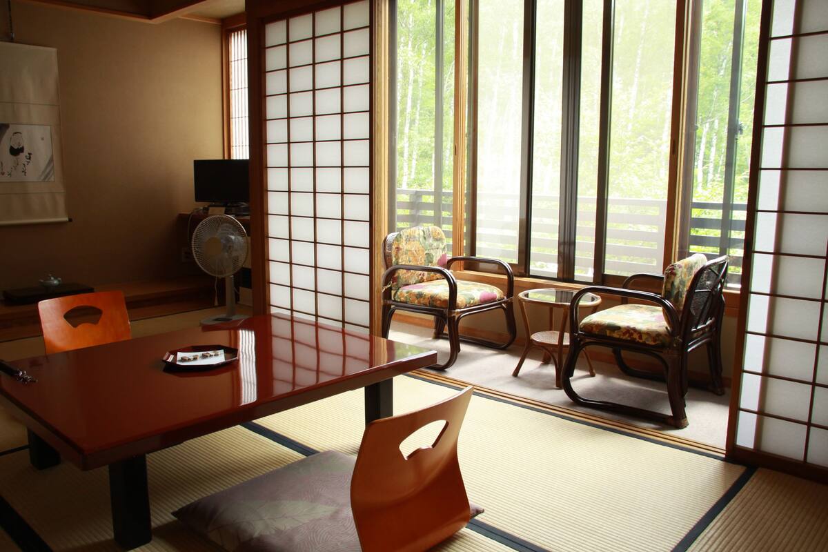 Una habitación japonesa tradicional con suelo de tatami, una mesa baja y dos sillas.