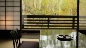 Una habitación con suelo de estera de tatami, una mesita baja con una bandeja y vistas a un bosque a través de una puerta corredera.