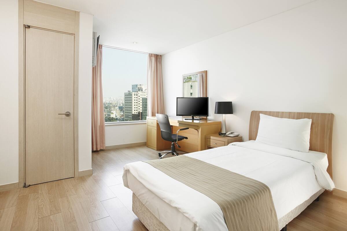 Ein Hotelzimmer mit Bett, Schreibtisch, Stuhl, Fernseher und Blick auf die Stadt.