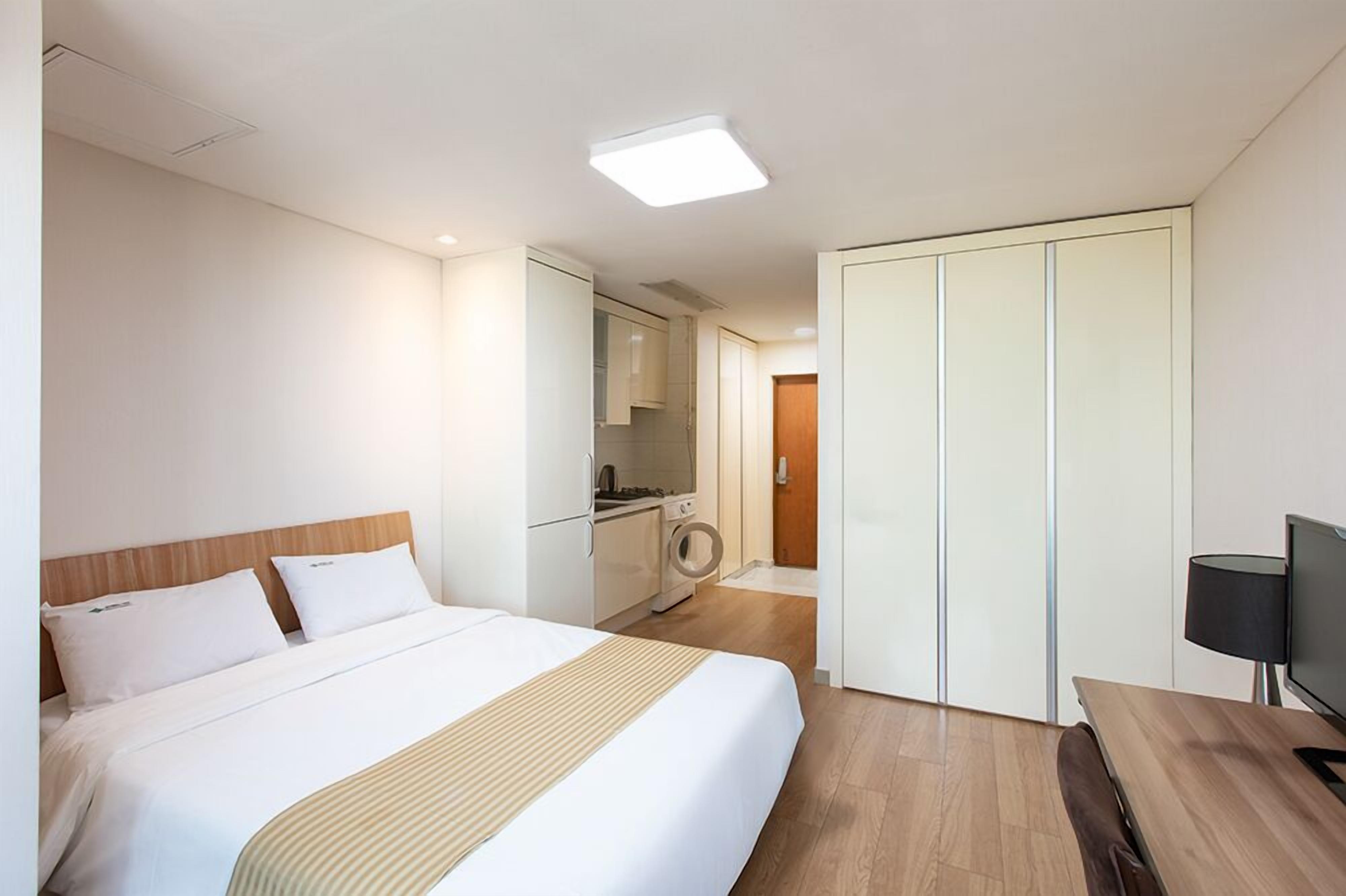 A hotel room with a bed, a desk, a television, a wardrobe, and a kitchenette.