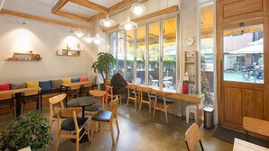 Una cafetería con muebles de madera, ventanas amplias y una planta.