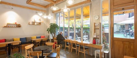 Een café met houten meubels, grote ramen en een plant.