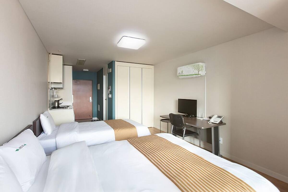 Ein Hotelzimmer mit zwei Betten, einem Schreibtisch, einem Stuhl, einem Fernseher und einem Kleiderschrank.
