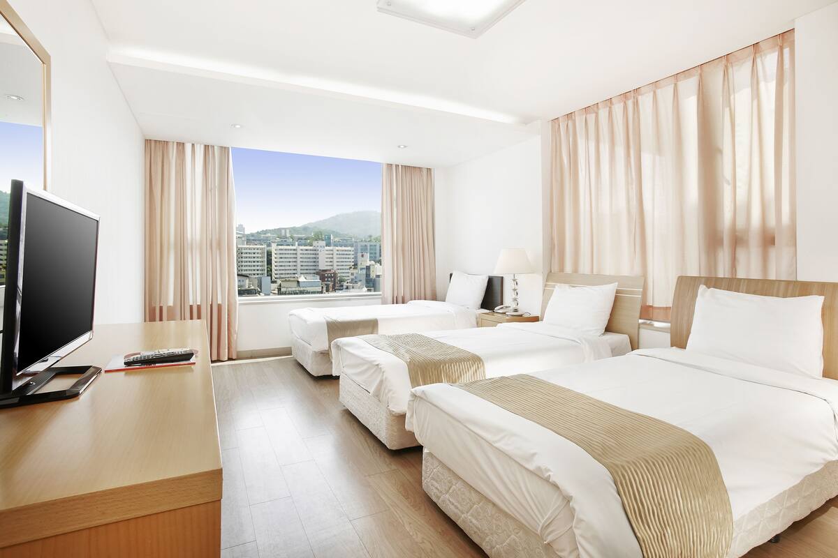 Ein Hotelzimmer mit zwei Betten, einem Fernseher und Blick auf die Stadt.