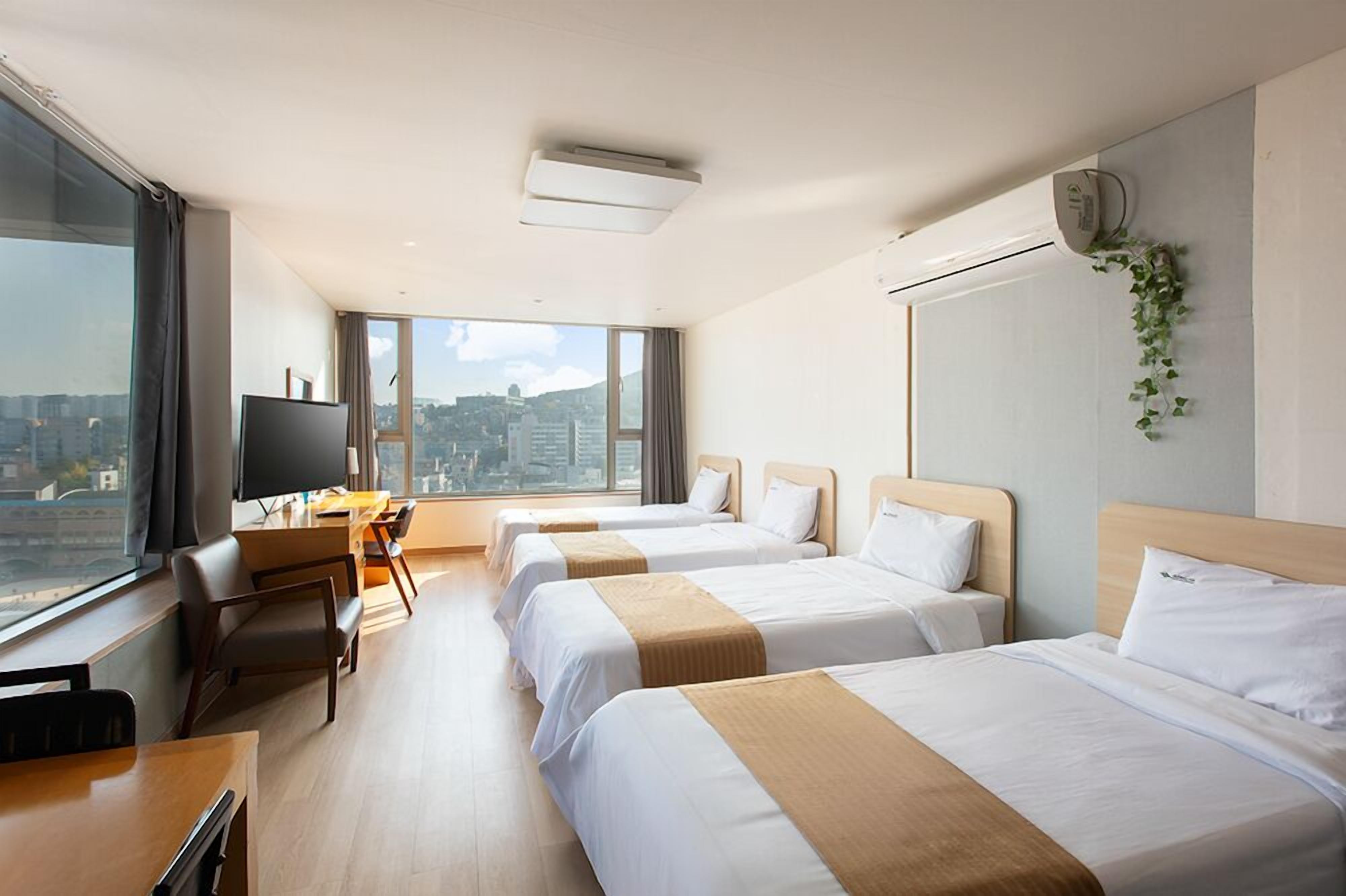 Une chambre d’hôtel avec trois lits, un bureau avec une télévision et une grande fenêtre donnant sur la ville.
