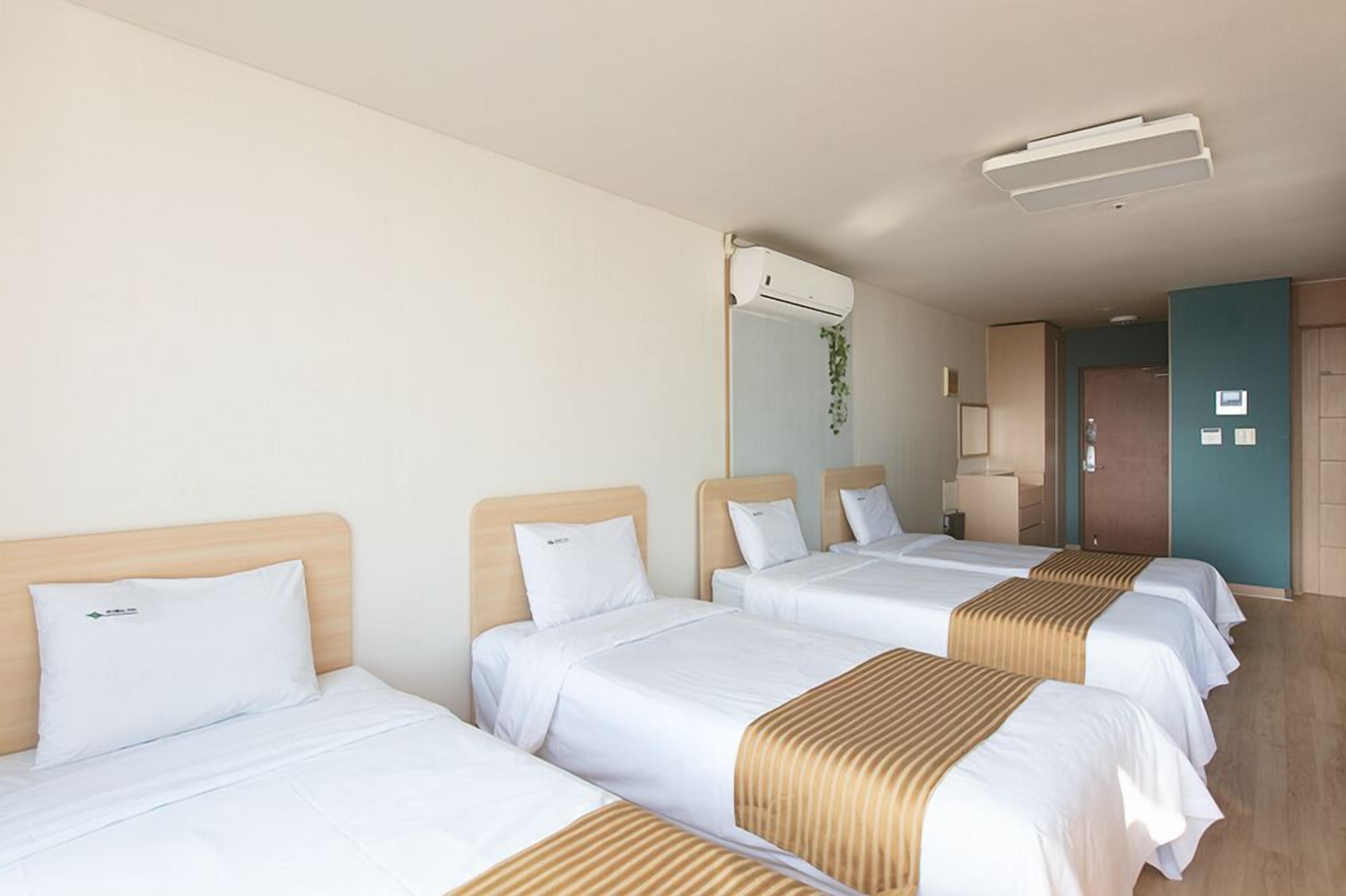 A hotel room with three beds, a ceiling fan, an air conditioning unit, and a door leading to another room.