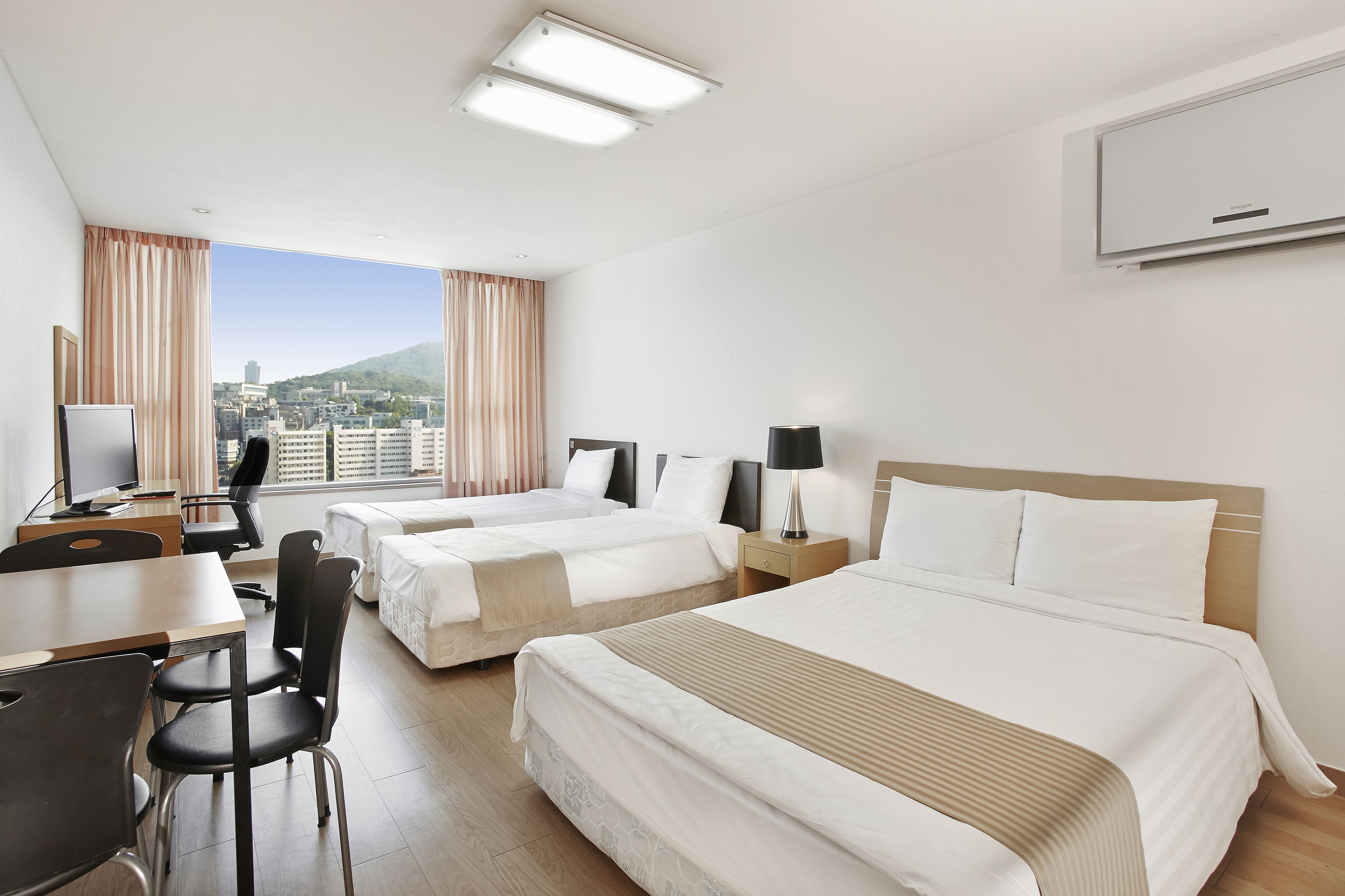 A hotel room with two beds, a desk, chairs, and a city view.