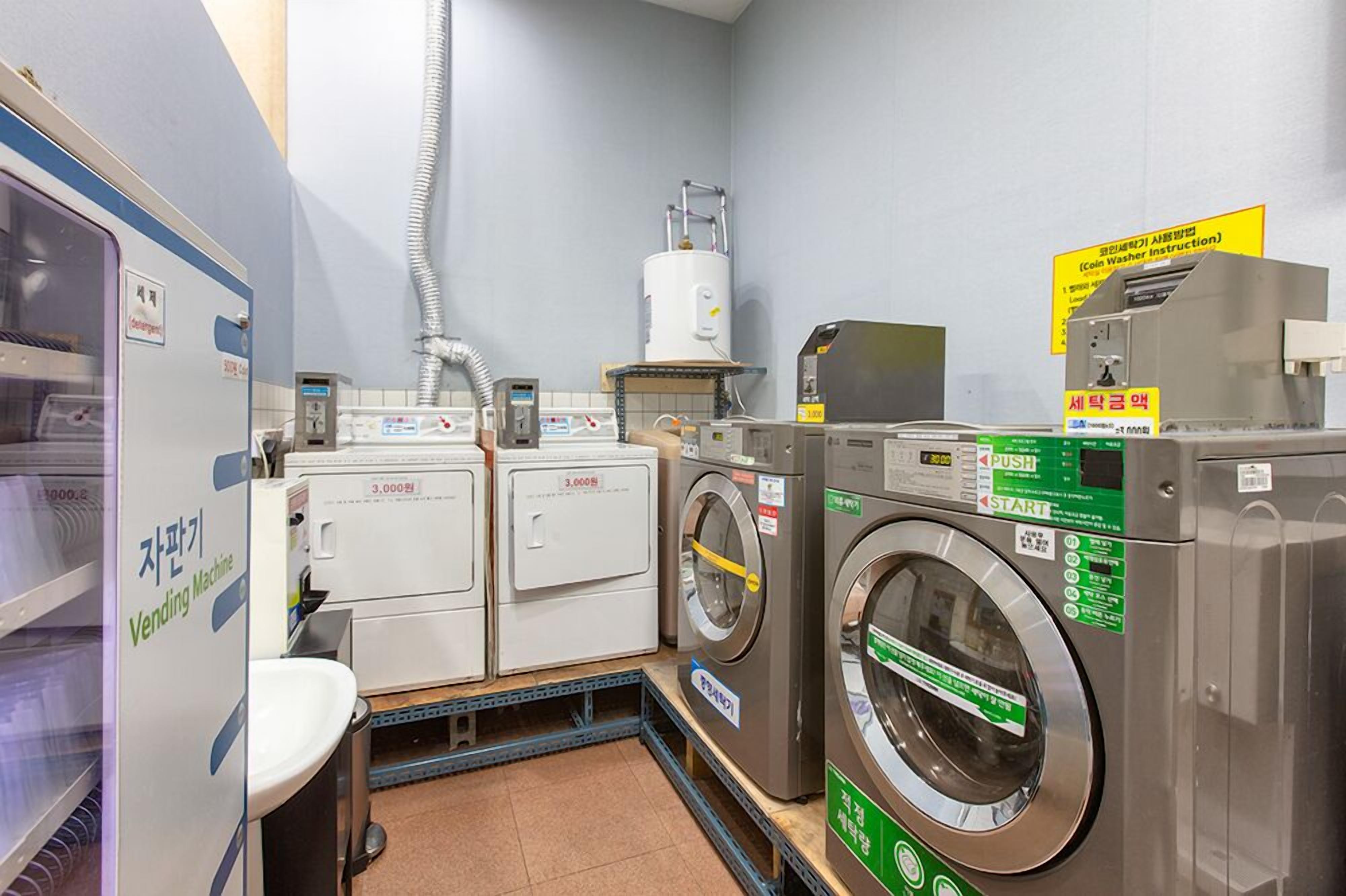 A laundromat with multiple washing machines and dryers, a water heater, and a sign with instructions.