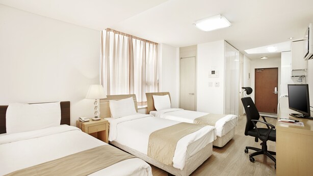 Une chambre d’hôtel avec deux lits, un bureau, une chaise, une télévision et une fenêtre avec des rideaux.