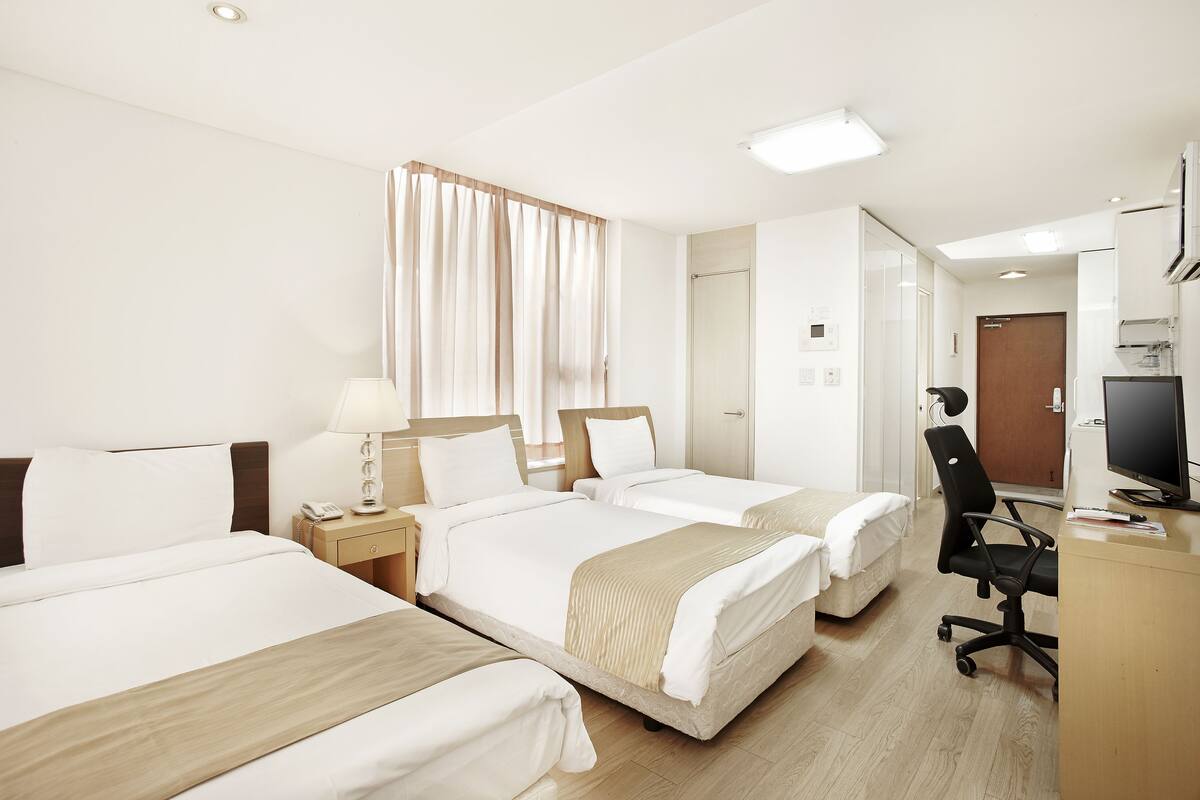 Ein Hotelzimmer mit zwei Betten, einem Schreibtisch, einem Stuhl, einem Fernseher und einem Fenster mit Vorhängen.