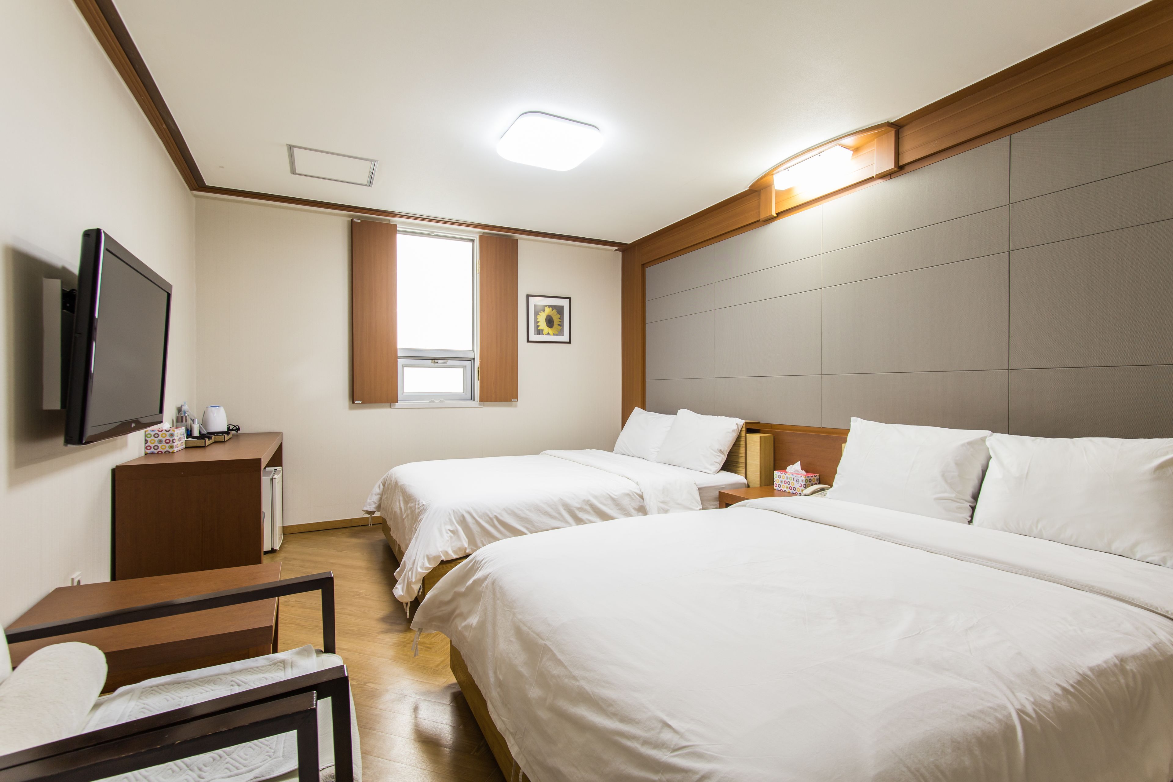A hotel room with two beds, a TV, a desk, and a window with blinds.